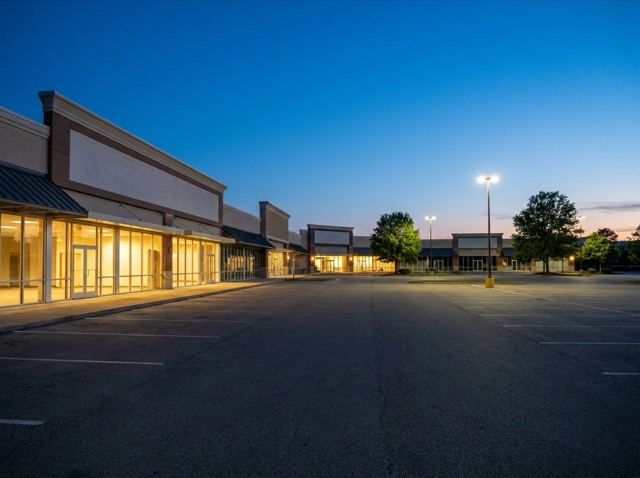 Lit storefronts and an empty parking lot at dusk