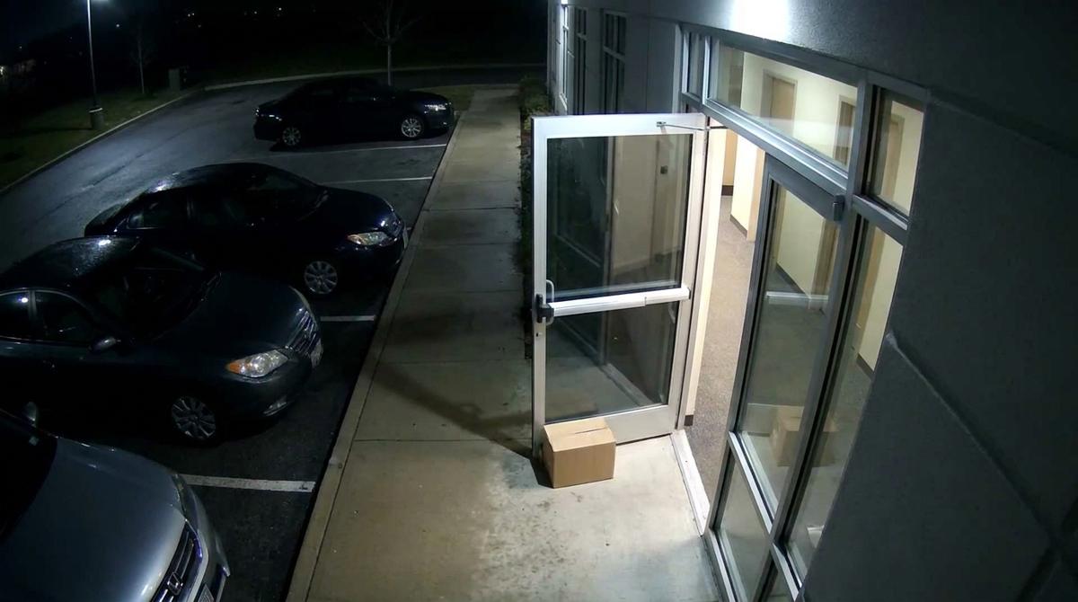A security camera view at night of an office building’s rear glass door propped open with a cardboard box