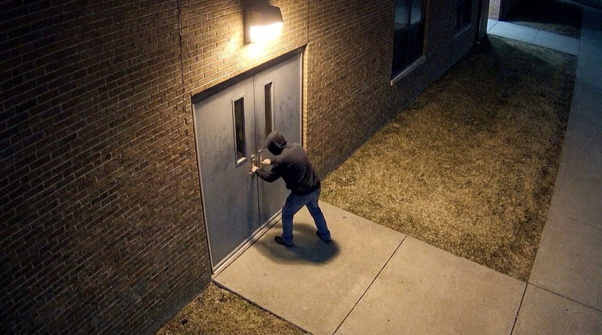 A security camera view at night of a person pulling on a school gym’s locked double doors