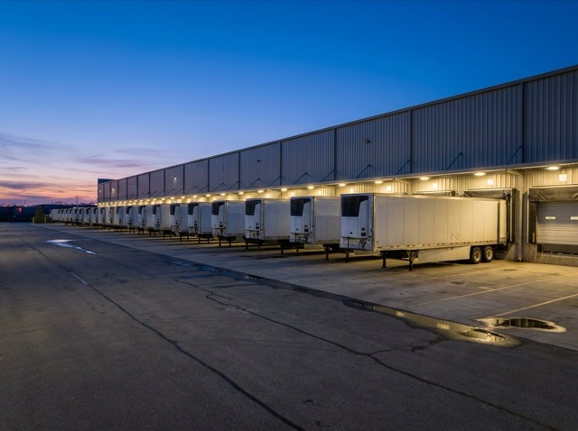 A distribution warehouse at dusk with trailers at the dock doors